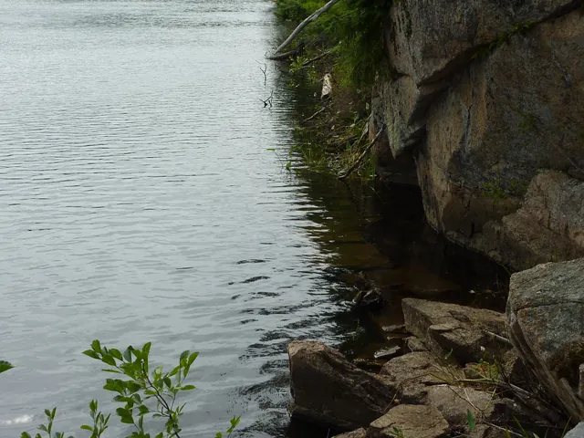 Clear water beside a granite cliff with flat stones visible just under the surface