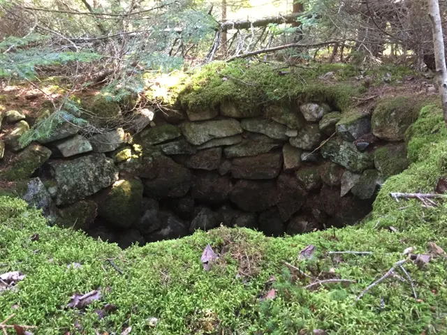 A round hole lined with dry-laid stone, edged with moss