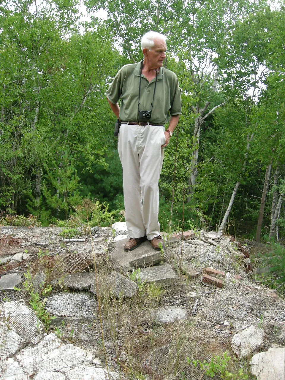 A white-haired crew member standing at the foot of a weathered stucco wall