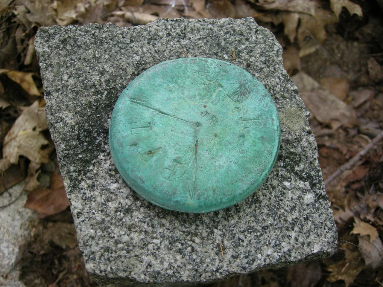 A green bronze survey disc set in a square granite block among dry leaves