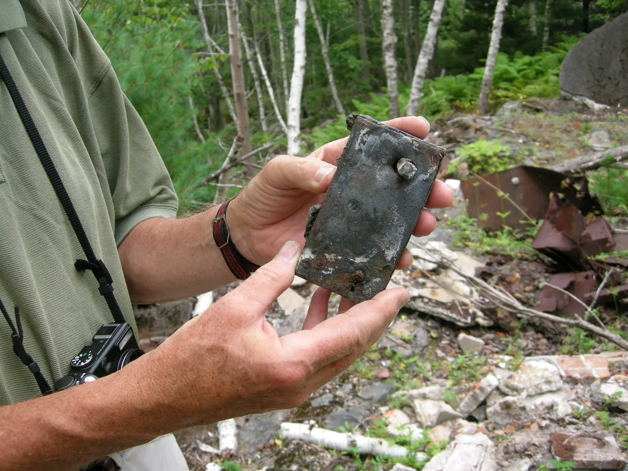 Hands holding a small rusted metal object above a debris field