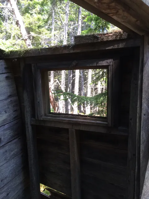 Inside the toilet building, looking at a square window in the board wall