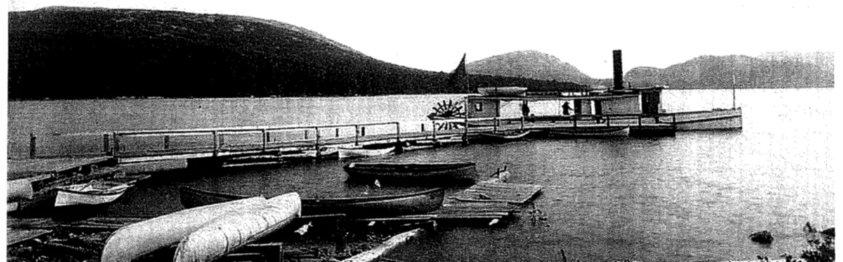 Small steamboat at a long wharf on a lake with mountains behind